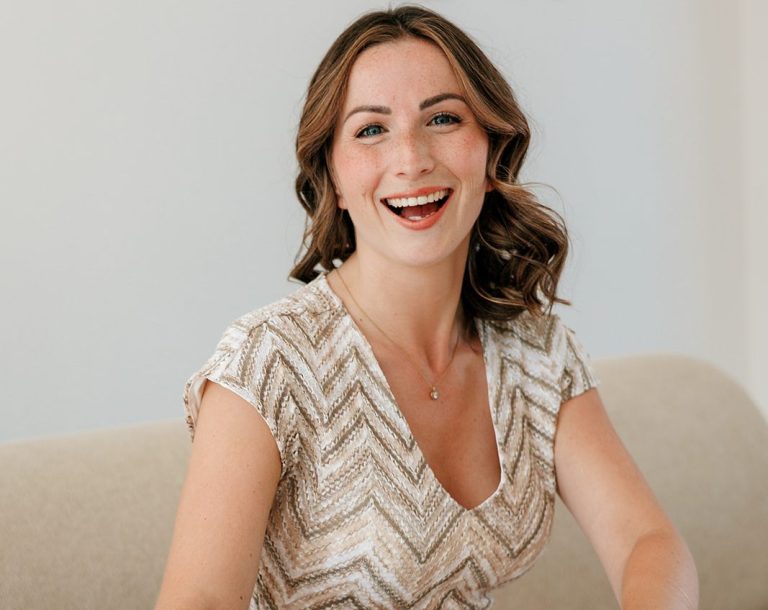 Coaching mit positiver Psychologie und Werten Lächelnde Frau mit lockigem Haar in festlichem Oberteil, sitzt auf einer hellen Couch.