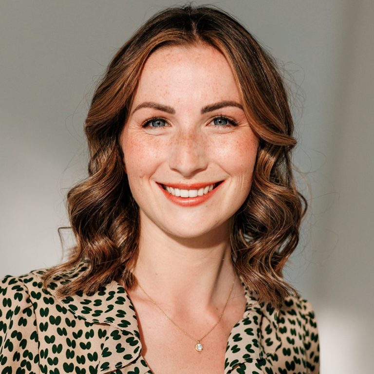 Life und Business Coaching Porträt einer lächelnden Frau mit lockigem Haar und blumigem Oberteil.